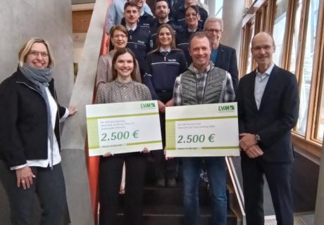 Auf einer Treppe stehen Vertreterinnen und Vertreter der Polizei Münster, der LVM und des Weißen Rings. Zwei Personen halten je ein Schild mit der Spendensumme von 2.500 EUR in den Händen.