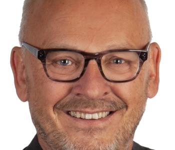 Das Foto zeigt einen lächelnden Mann mit Brille und schwarzem Jacket im Portrait.